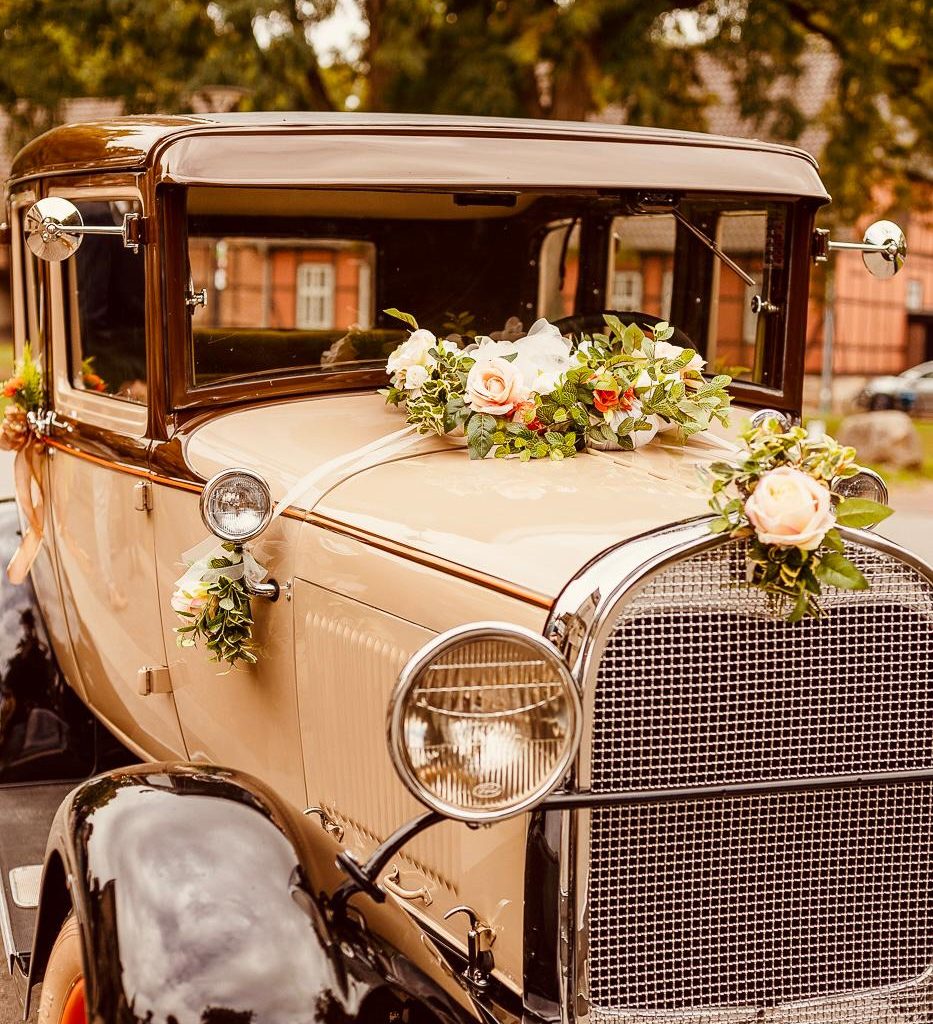 Barauttaxi wartet vor dem Hotel auf das Paar das Brauttaxi mit Blumenarrangements auf der Motorhaube.